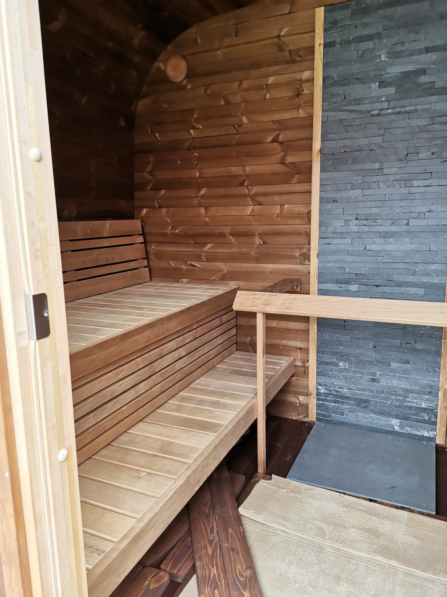 Sauna exterior Cubos de madera y piedra con bancos interiores.