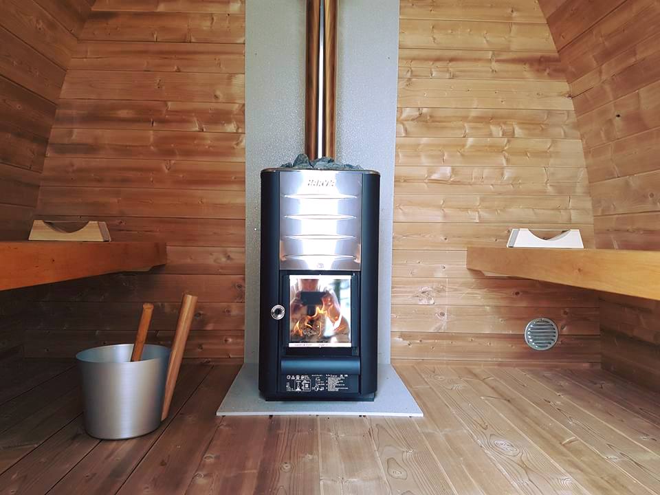 Outdoor sauna pod with wood-burning stove inside the room.