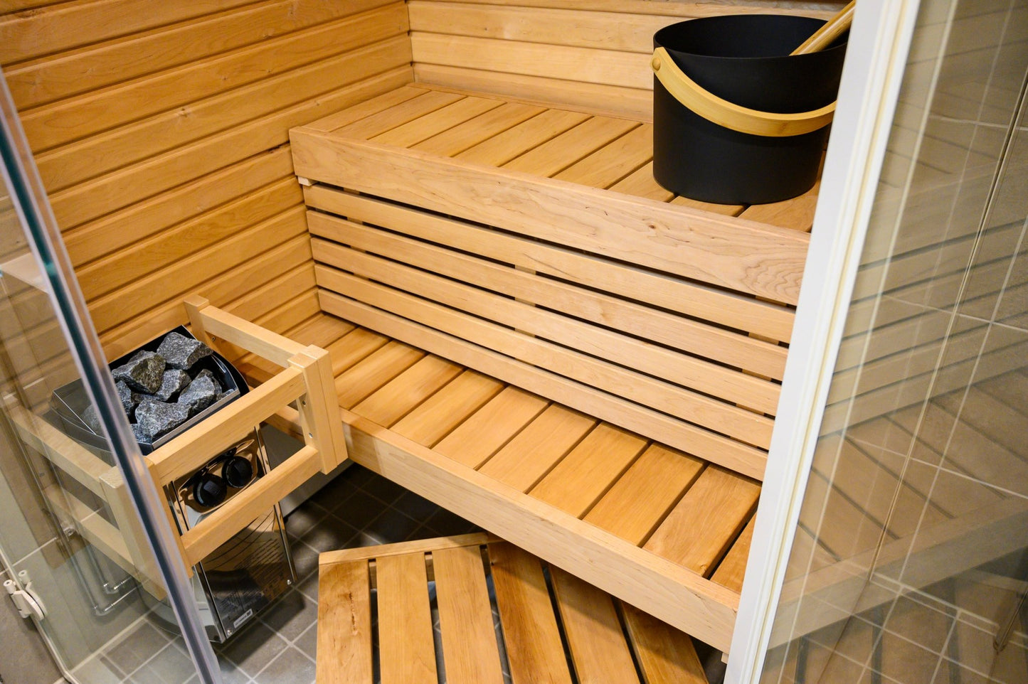 Sirius Corner sauna with wooden bench and black bucket.