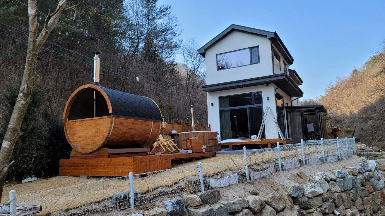 Sauna esterna Barrel 250 in giardino con botte di legno.