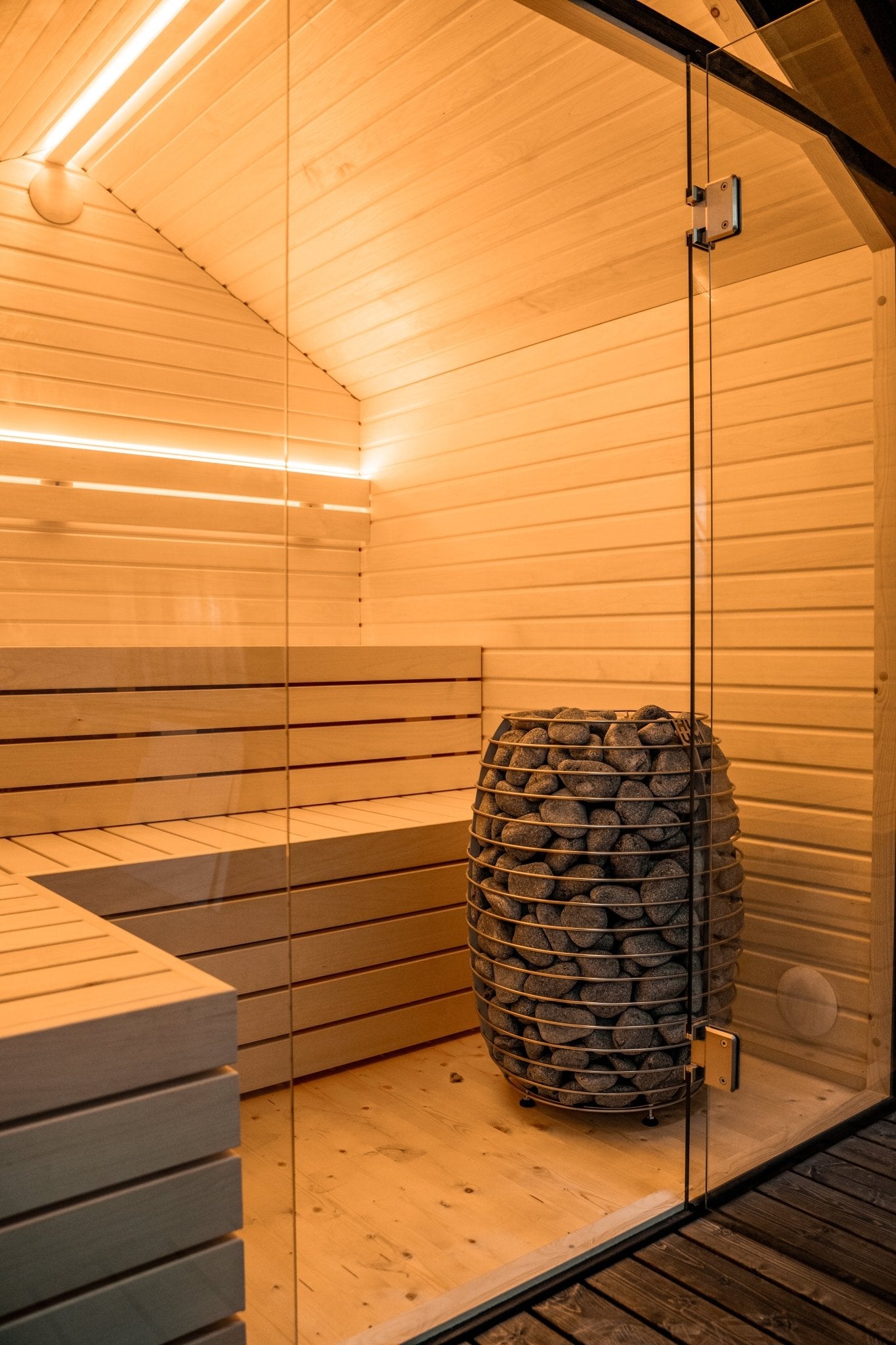 Sauna exterior Lumi con puerta de cristal y piedras visibles.