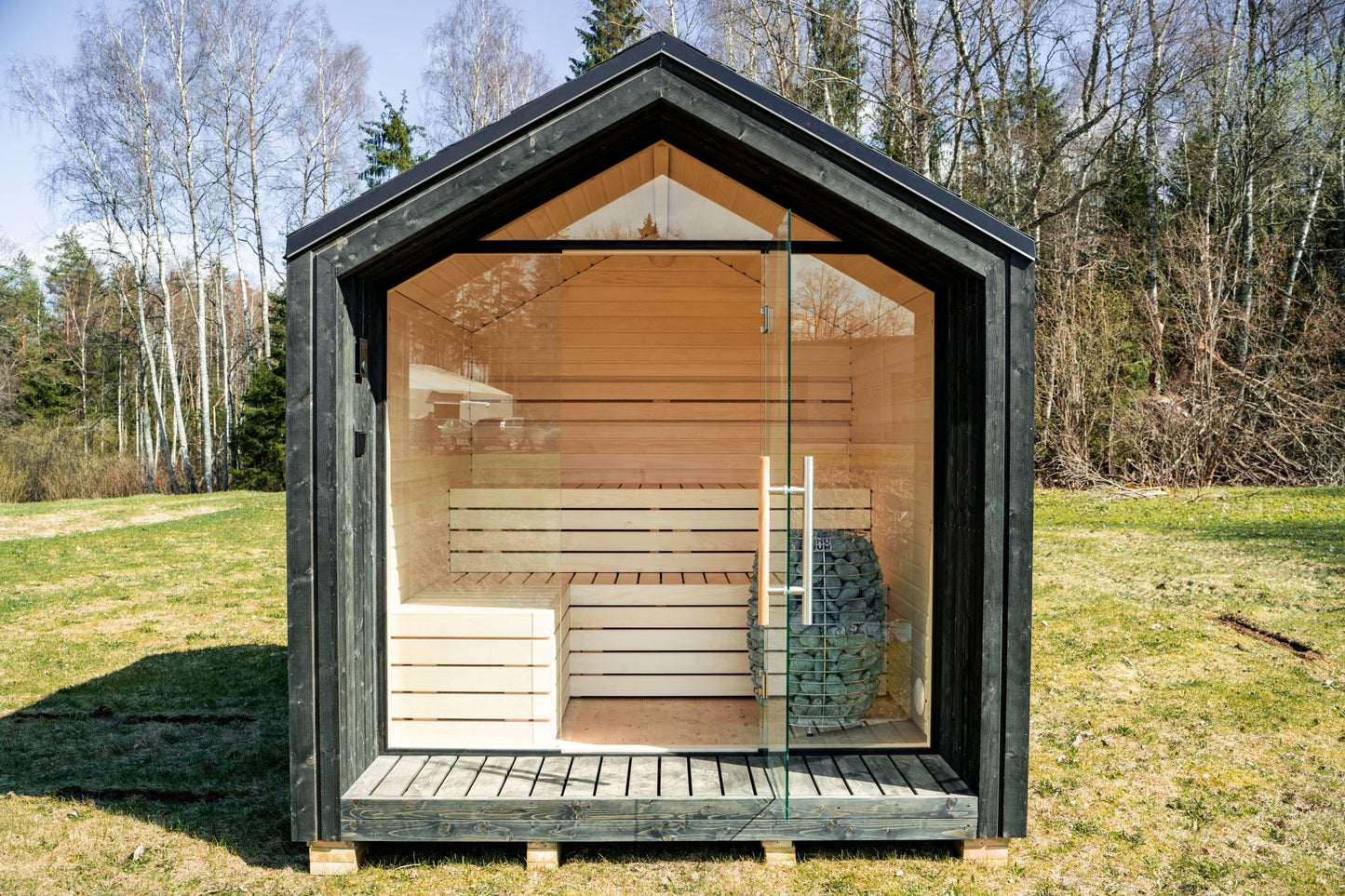 Sauna exterior Lumi aislada con puerta de cristal en una zona de césped.