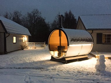 Sauna de barril em ambiente de neve com luz interior.