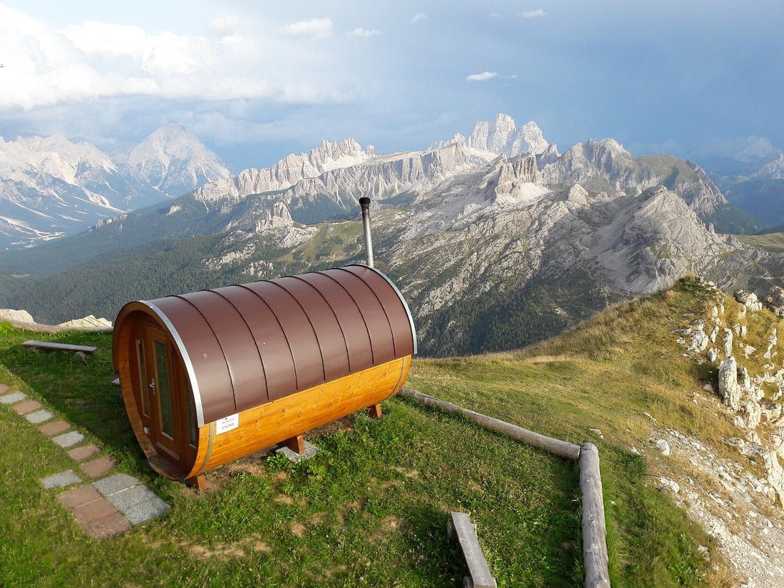 Sauna de barril em colina com montanhas ao fundo.