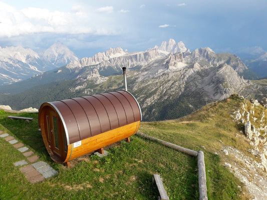 Sauna de barril em colina com montanhas ao fundo.