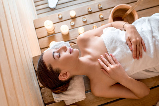 Mulher relaxando em sauna com velas, próximo a um balde d'água.